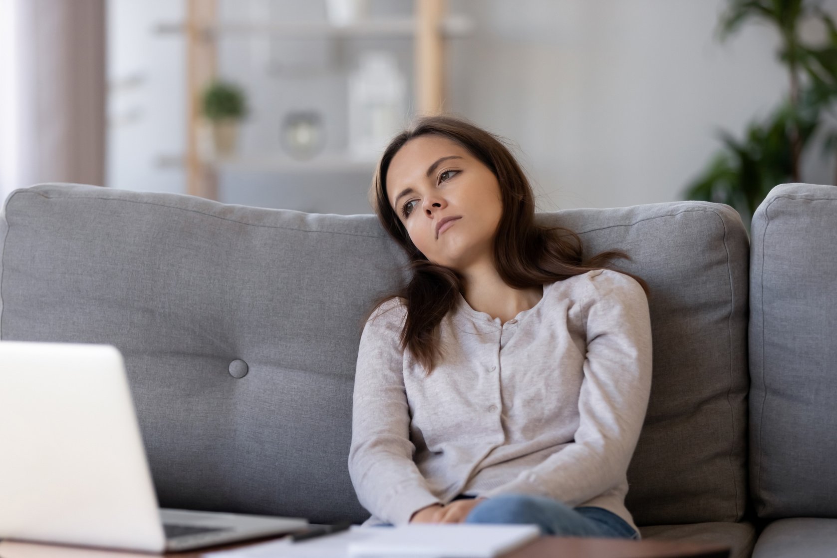 Tired apathetic teenager looking away sitting on couch feeling demotivated